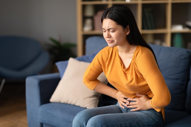 Ongelukkige Aziatische dame die binnenshuis worstelt met menstruatiekrampen en buikpijn