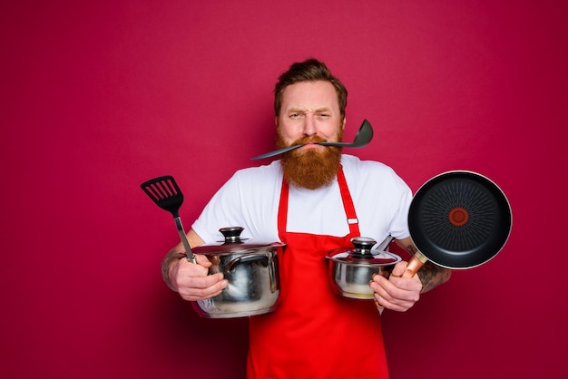 Ongelukkige chef-kok met baard en rode schort is klaar om te koken