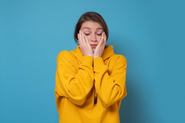 Ongelukkige jonge vrouw die handen op het gezicht houdt en een plan probeert te maken om haar problemen op te lossen Studio-opname op blauwe muur