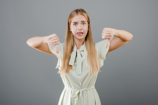 Ongelukkige teleurgestelde jonge vrouw die thubms tonen die over grijs wordt geïsoleerd