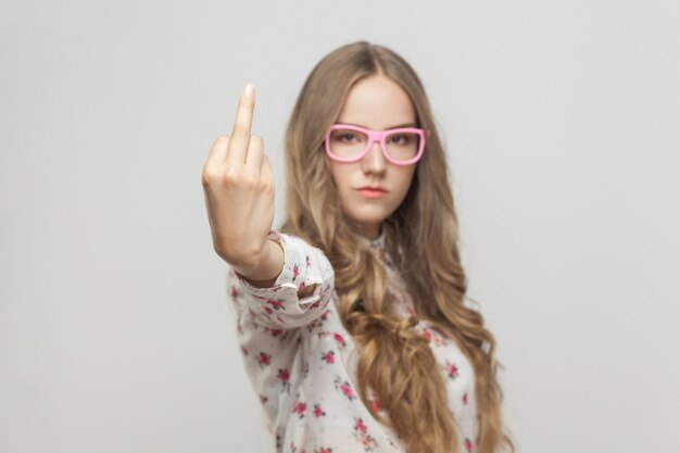 Ongelukkige vrouw, die een fuck-bord toont op de camera. Focus bij de hand. Binnenopname, grijze achtergrond