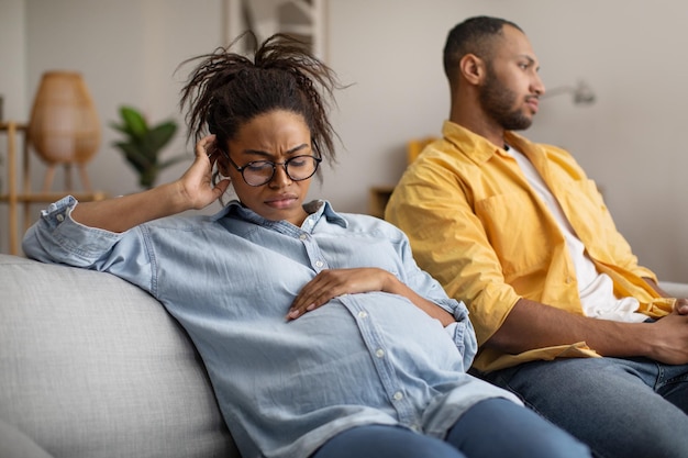 Ongelukkige zwangere zwarte vrouw zit bij onverschillige echtgenoot thuis