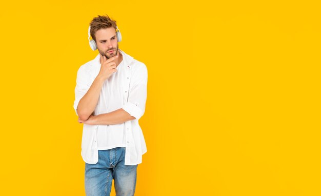 Ongeschoren jonge man in koptelefoon op gele achtergrond, modern apparaat.