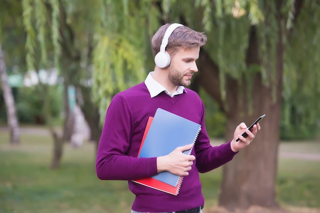 Ongeschoren man met notitieboekje en muziek luisteren in oortelefoons van smartphone, onderwijs.