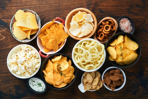 Foto ongezond voedsel of snacks alle klassieke aardappelsnacks met pinda's, popcorn en uienringen en gezouten pretzels in komplaten op oude houten achtergrond ongezond voedsel voor figuurharthuidtanden