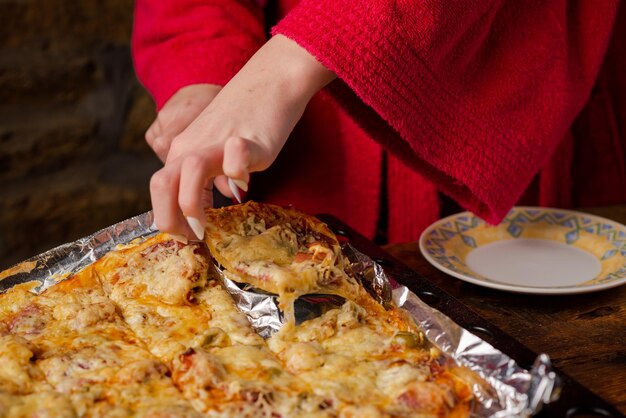 Onherkenbaar meisje pakt stuk zelfgemaakte pizza Vrouwhand met lange nagels houdt keukenspatel vast