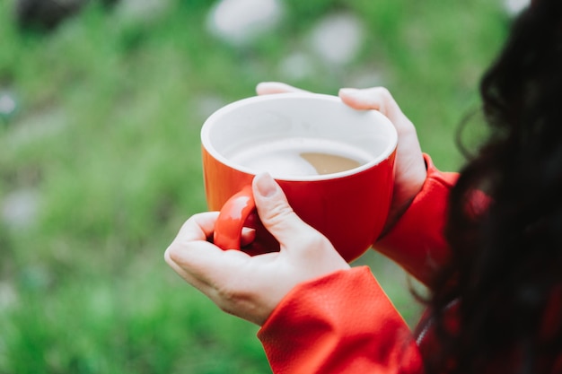 Onherkenbaar persoon, gekleed in een rood leren jack en met een rode mok met warme koffie in de natuur