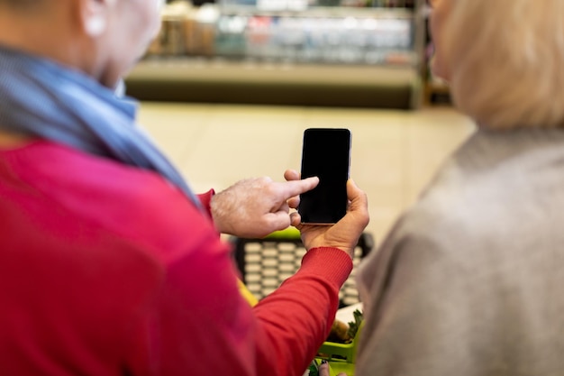 Onherkenbaar senior koppel dat smartphone gebruikt tijdens het winkelen