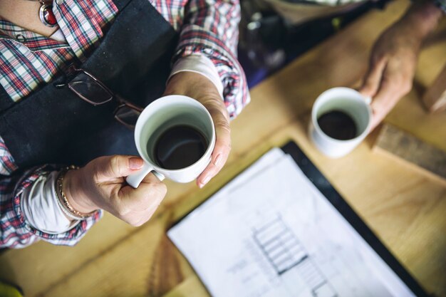 Onherkenbaar senior koppel pauzeert voor koffie in hun timmerwerkplaats