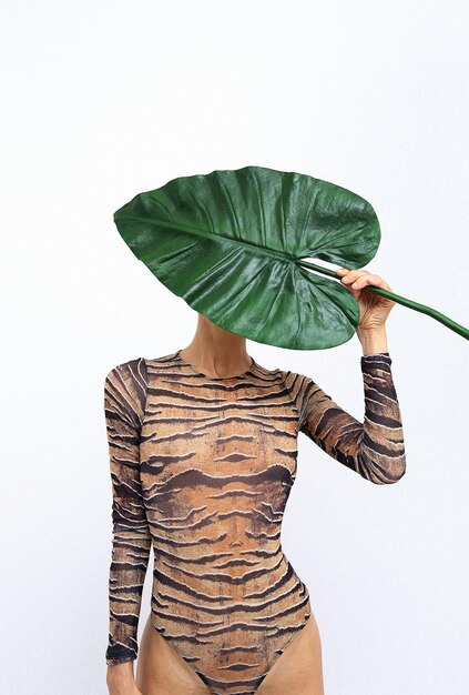 Onherkenbaar wijfje dat palmblad in tijgerbodysuit houdt. tropisch jungle wild creatief concept. eco minimalistische modedetails