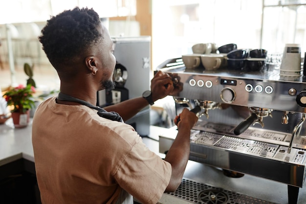 Onherkenbare Afro-Amerikaanse barista die instellingen op professionele koffiemachine aanpast voor het maken van...