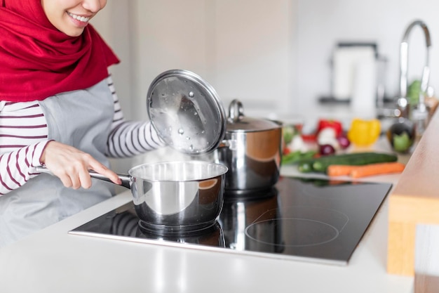 Onherkenbare Arabische vrouw huisvrouw koken op elektrisch fornuis thuis