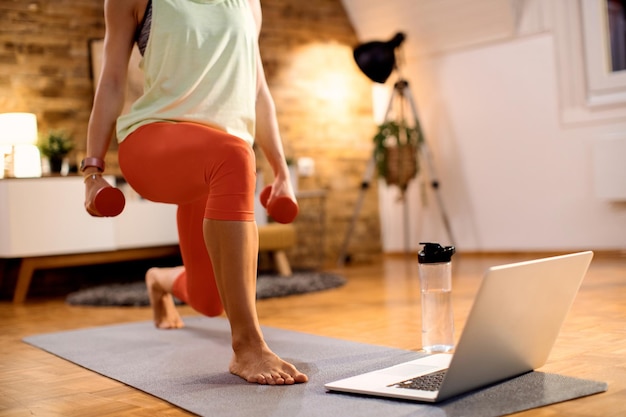 Onherkenbare atleet die dumbbells gebruikt tijdens lunges tijdens thuistraining