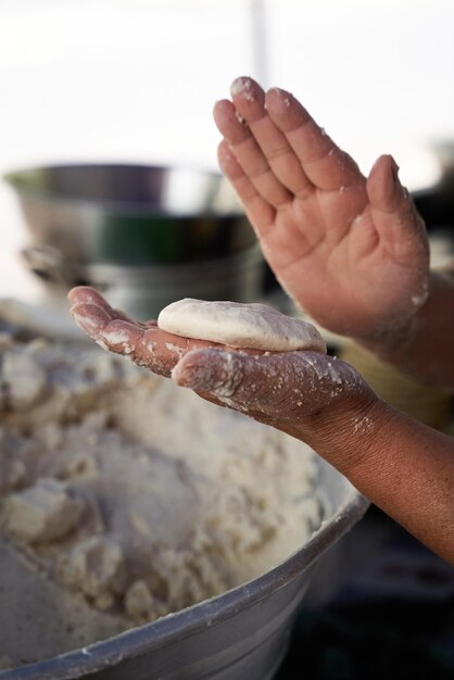 Foto onherkenbare bejaarde vrouw bereidt maïs tortillas met de hand op een grill in haar bescheiden straatkeuken