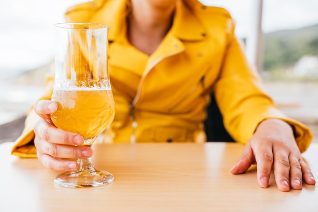 Onherkenbare blanke vrouw in gele leren jas die een glas bier drinkt