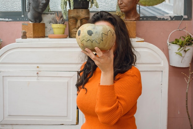 onherkenbare blanke vrouw thuis die haar gezicht bedekt met halloween-pompoen