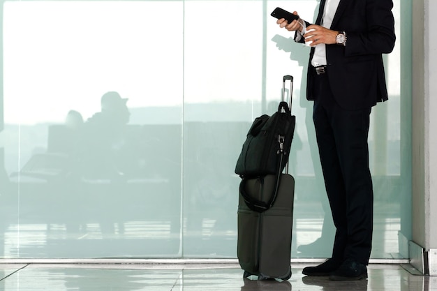 Foto onherkenbare directeur met zijn mobiele telefoon een koffie en zijn koffer te wachten op de luchthaven