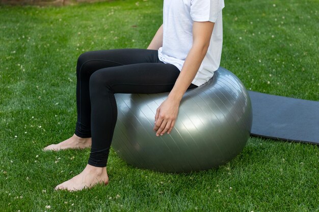 Onherkenbare fitness slanke man zittend op een balace bal tijdens het trainen op blote voeten in de tuin vers gras