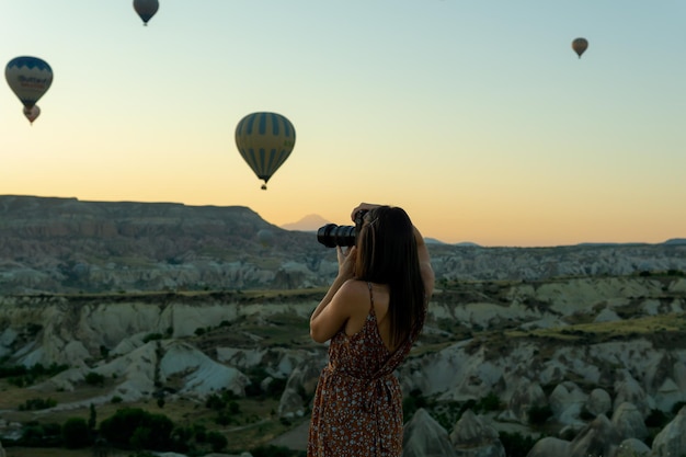 Onherkenbare fotograaf die een foto maakt van het landschap van de liefdesvallei en de typische heteluchtballonnen van Cappadocië die bij zonsopgang vliegen