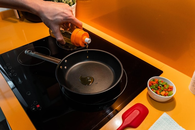 Onherkenbare hand die olijfolie in koekenpan gooit in oranje keuken