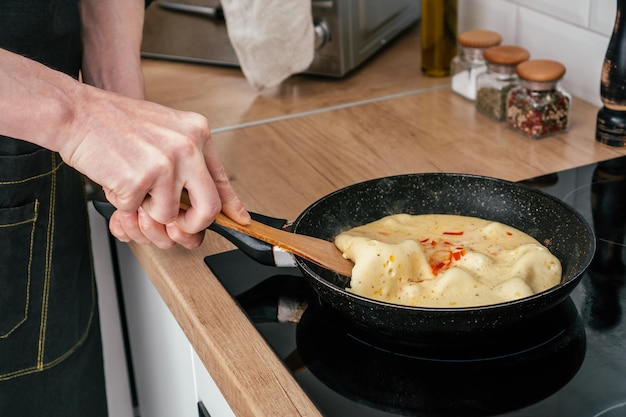 Onherkenbare handen van de mens die een verse omelet uit de koekenpan haalt met een houten peddel op een zwart elektrisch fornuis