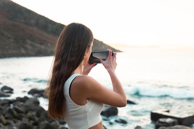 Onherkenbare jonge blanke vrouw die een foto maakt van een strand en de zee met een smartphone