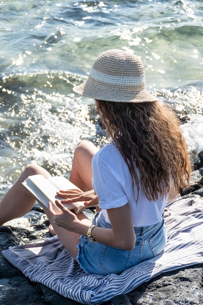 Onherkenbare jonge vrouw die aan zee een boek leest