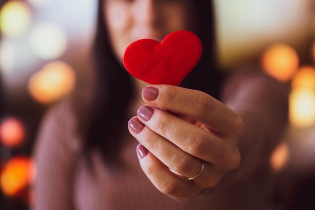 Onherkenbare jonge vrouw die met één hand een klein rood hart vasthoudt