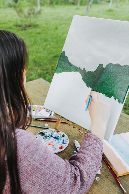 Onherkenbare jonge vrouwelijke kunstenares die haar eigen berglandschap schildert met olieverf op een doek. Amateur