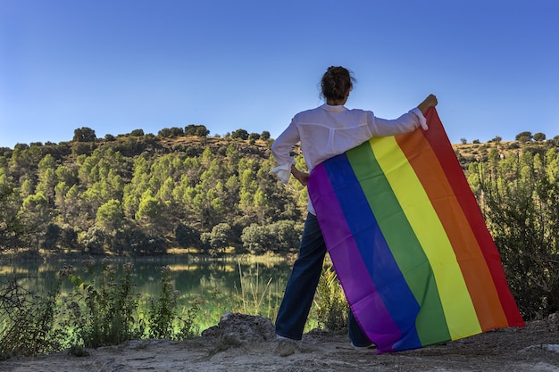 Onherkenbare lesbische vrouw van middelbare leeftijd die de Gay Rainbow Flag vasthoudt aan het meer buitenshuis. Vrijheidsconcept