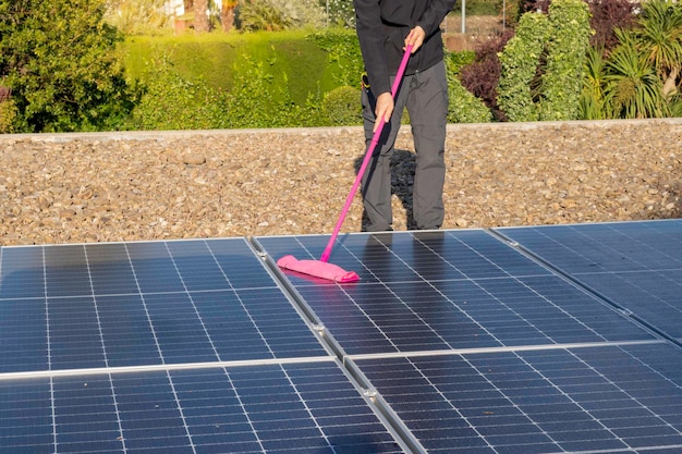 Onherkenbare man die met een dweil een zonnepaneelbroek op het dak van het huis schoonmaakt
