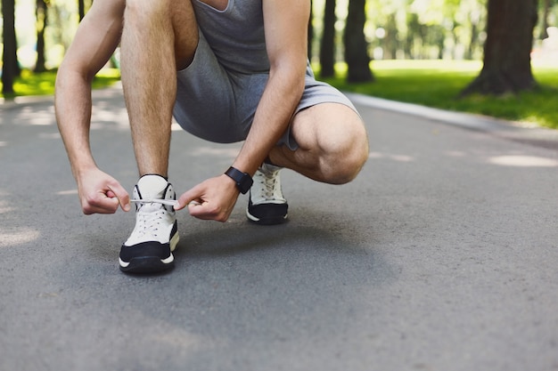 Onherkenbare man die schoenveters aan sneakers bindt voordat hij gaat rennen, zich klaarmaakt om te joggen in het park, close-up, kopieerruimte, bijsnijden