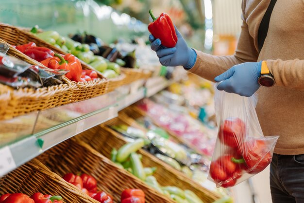 Onherkenbare man in rubberen handschoenen chosses rode peper in de supermarkt tijdens het uitbreken van een coronavirus longontsteking