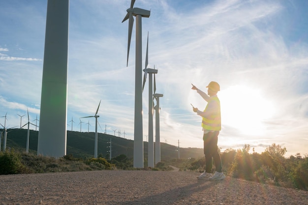 Onherkenbare mannelijke arbeider wijst naar windturbines bij zonsondergang