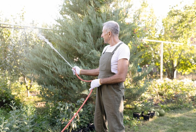 Onherkenbare mannelijke senior tuinman die de planten in de tuin water geeft met behulp van een rubberen slang die zorgt voor