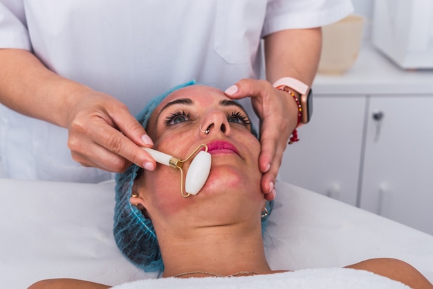 Onherkenbare schoonheidsspecialist die een massage uitvoert met jaderoller voor volwassen vrouw in beauty spa