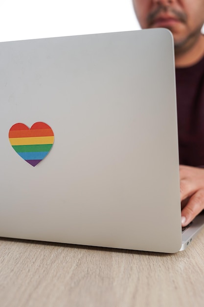 Onherkenbare Spaanse man aan het werk met zijn computer die een hart heeft met de kleuren LGBTQ