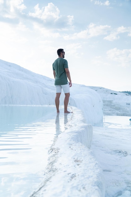 Onherkenbare toerist met baard en zonnebril starend naar de horizon met zijn voeten verzonken in de thermale baden van Pamukkale