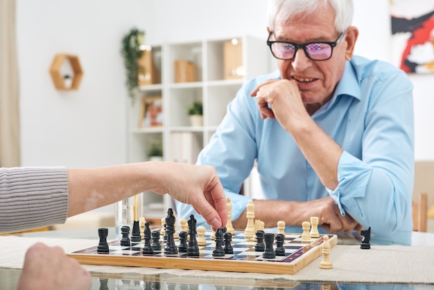 Onherkenbare vrouw aan tafel zitten en schaken met gepensioneerde senior man in glazen in verpleeghuis