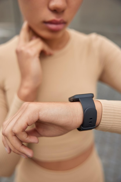 Onherkenbare vrouw controleert pols na intensief hardlopen houdt hand op nek gericht op smartwatch leidt actieve levensstijl gekleed in sportkleding poses tegen onscherpe achtergrond Blijf fit en gezond