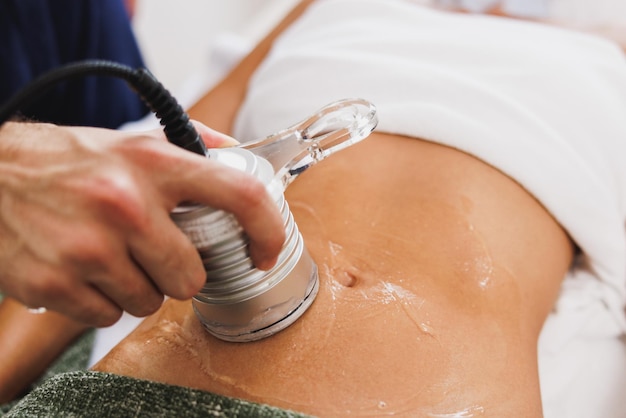 Onherkenbare vrouw die een ultrasone cavitatiebehandeling krijgt om vet op de buik te verminderen in de schoonheidssalon.