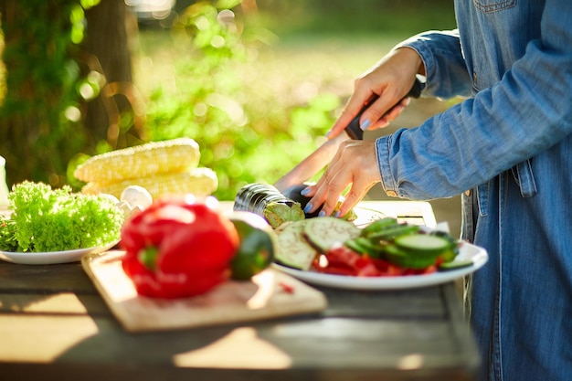 Onherkenbare vrouw die verse auberginegroenten op een houten bord snijdt tijdens weekendbarbecue in de tuin, buiten, voorbereiden op grillen, zomerfamiliepicknick, eten in de natuur.