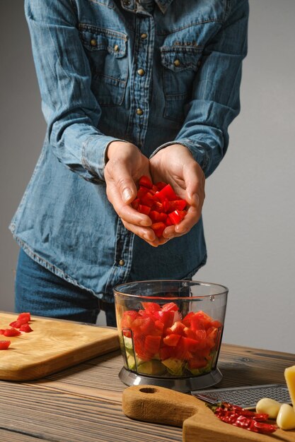 Onherkenbare vrouw giet fijn gesneden paprika in de blenderbak