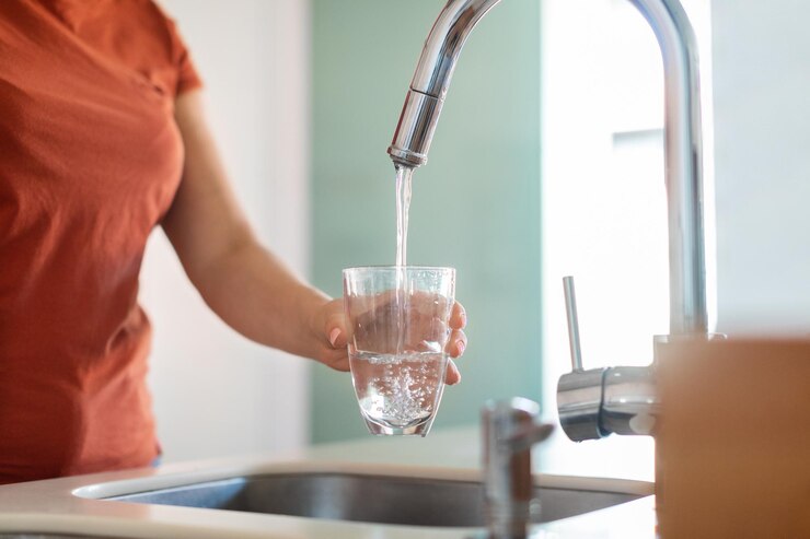 Onherkenbare vrouw glas vullen met water uit de kraan in de keuken