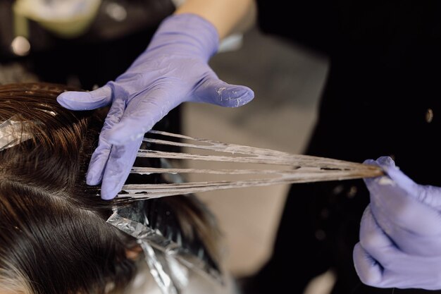 Onherkenbare vrouw kapper colorist houdt streng lang haar vast en verdeelt haarverf met vinger