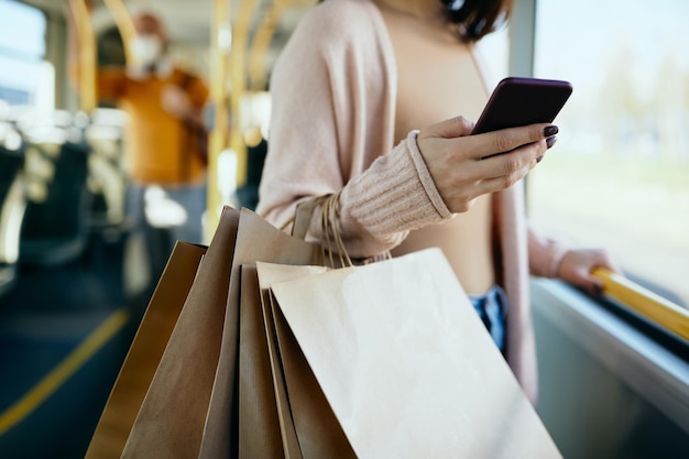 Onherkenbare vrouw met boodschappentassen die sms't aan de telefoon tijdens het woon-werkverkeer met de bus