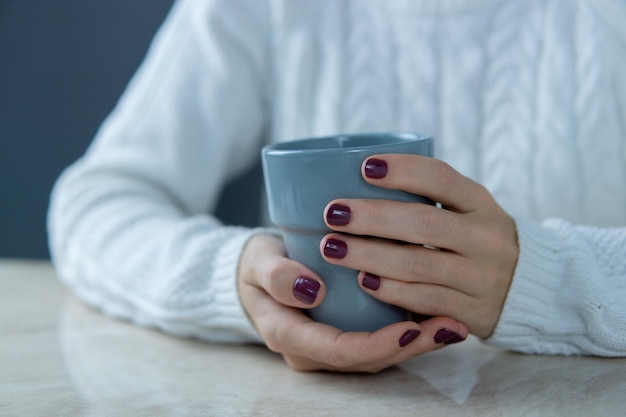 Onherkenbare vrouw met een kopje in haar handen leunend op de tafel