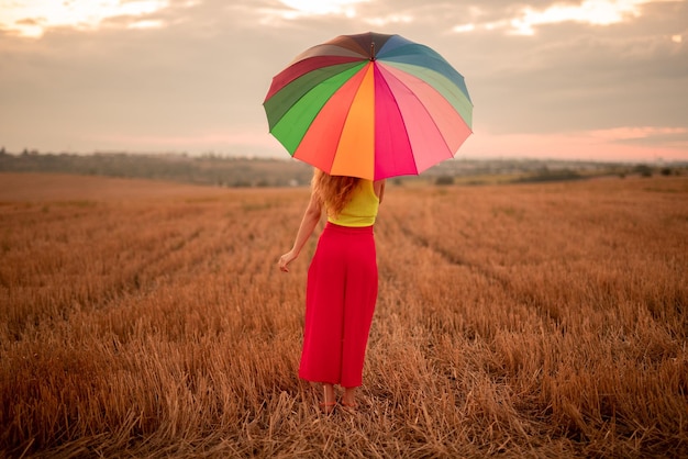 Onherkenbare vrouw met paraplu in veld tijdens zonsondergang