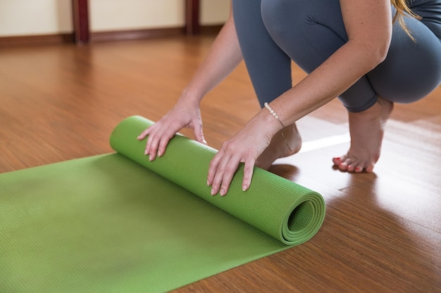 Onherkenbare vrouw rolt groene mat op voor training Slank meisje in sportkleding eindigt met yoga fitness