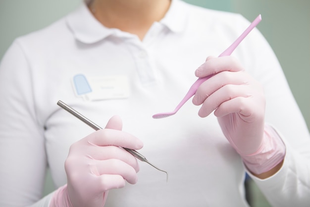 Onherkenbare vrouwelijke tandarts die medische rubberhandschoenen draagt, die tandhulpmiddelen houdt
